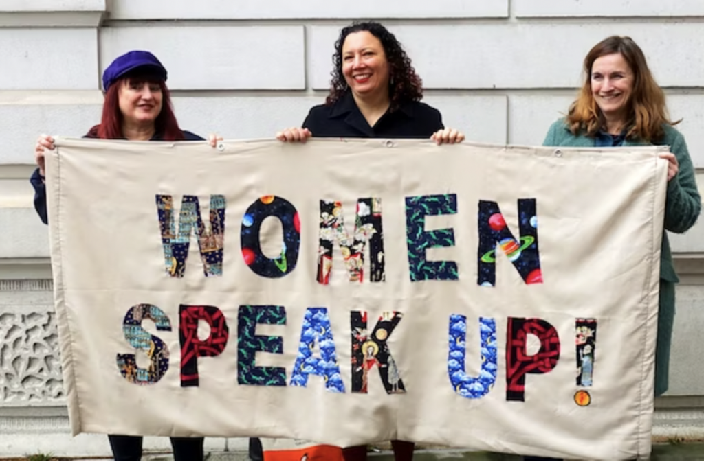 Three women holding banner "Women speak up!"