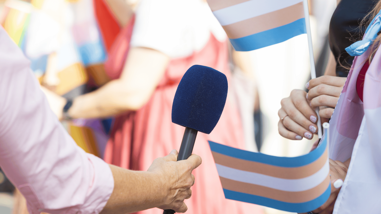 Someone holding a microphone up to a person holding a trans flag